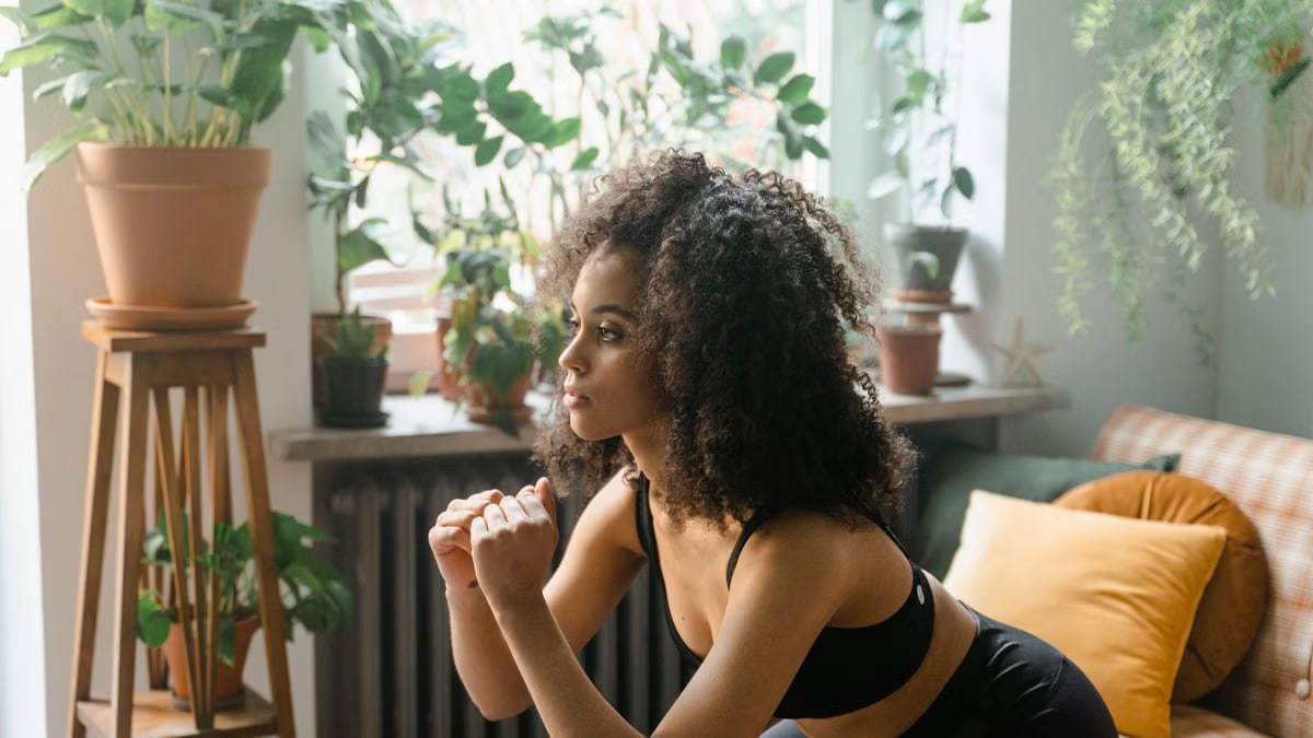 African American woman doing squats indoors surrounded by lush houseplants.